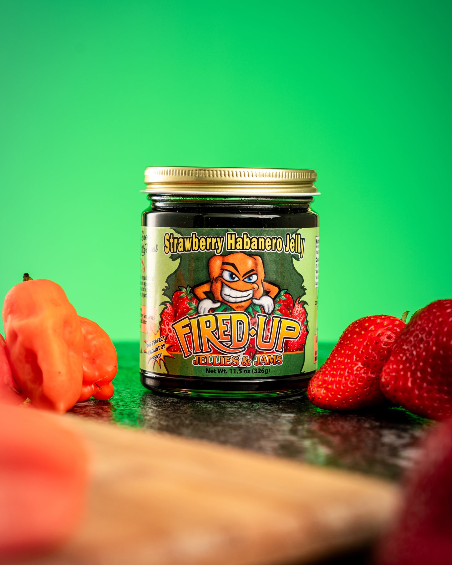 Lifestyle photo of Strawberry Habanero Jelly nestled with strawberries and habaneros with green Background