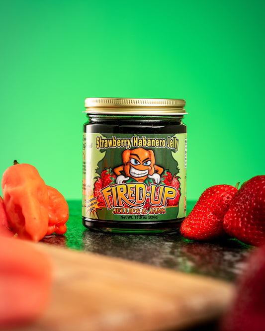 Lifestyle photo of Strawberry Habanero Jelly nestled with strawberries and habaneros with green Background