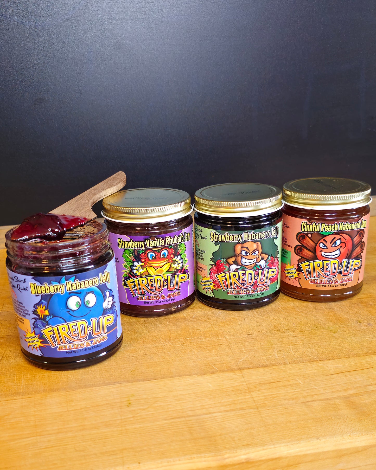 Blueberry Habanero Jelly with jelly on wooden knife resting on top of jar, Strawberry Vanilla Rhubarb Jam, Strawberry Habanero Jelly, Cinnful Peach Habanero Jam