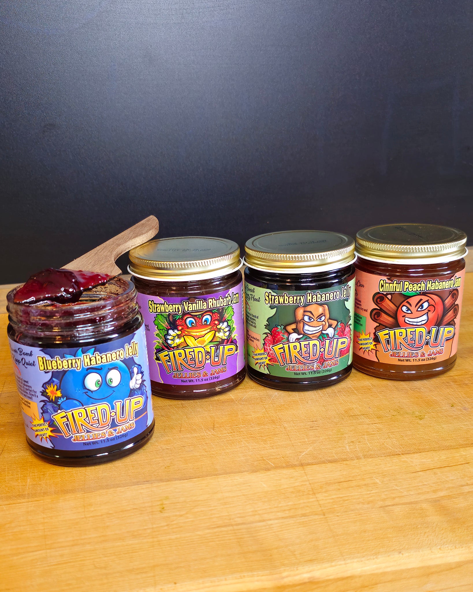 Blueberry Habanero Jelly with jelly on wooden knife resting on top of jar, Strawberry Vanilla Rhubarb Jam, Strawberry Habanero Jelly, Cinnful Peach Habanero Jam