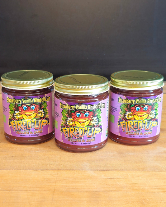 Three jars of 'Fired Up' strawberry vanilla rhubarb jam on a wooden surface with a black background.